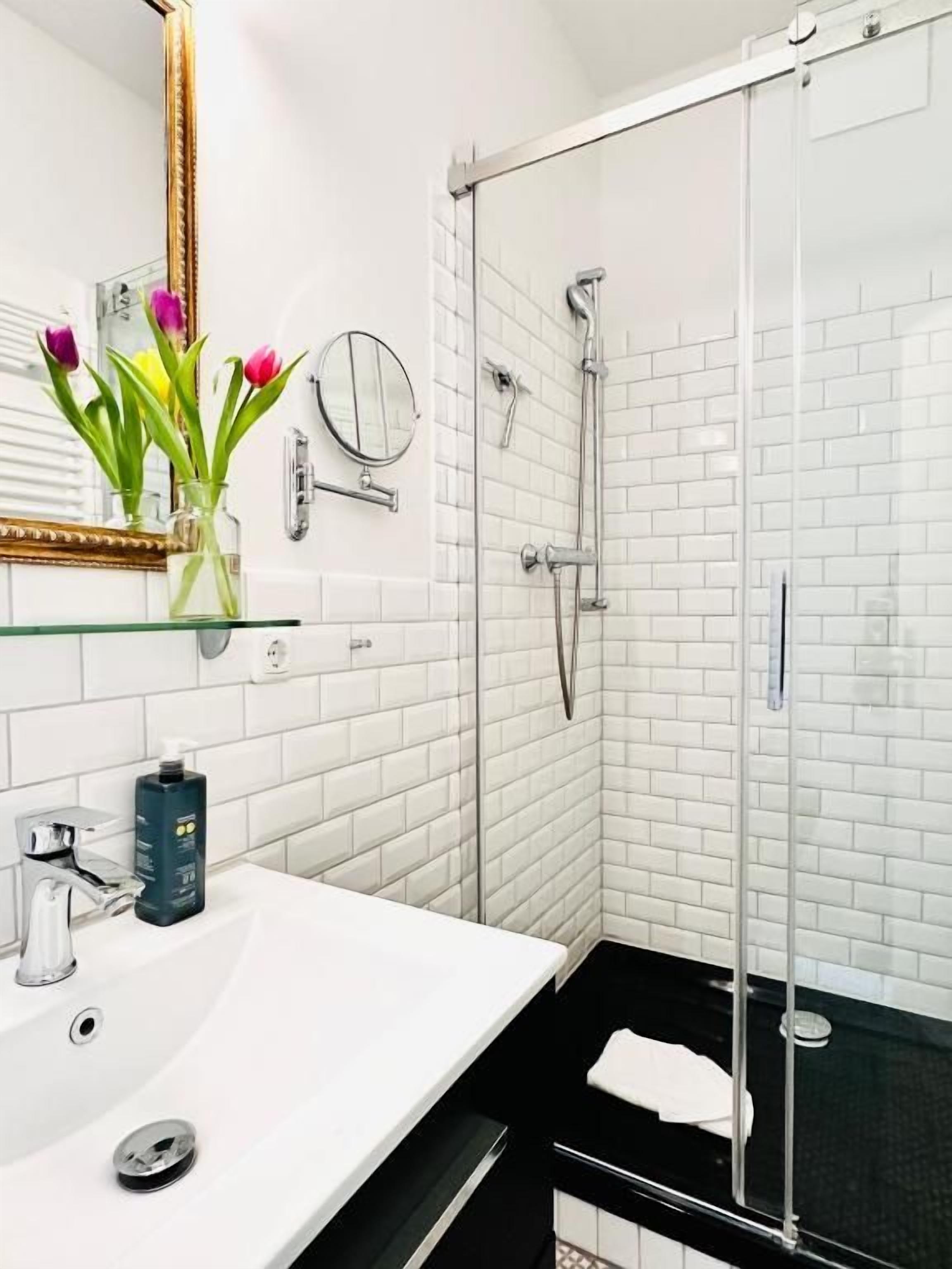 A modern bathroom with a white sink, a glass shower enclosure, and a mirror with a gold frame.