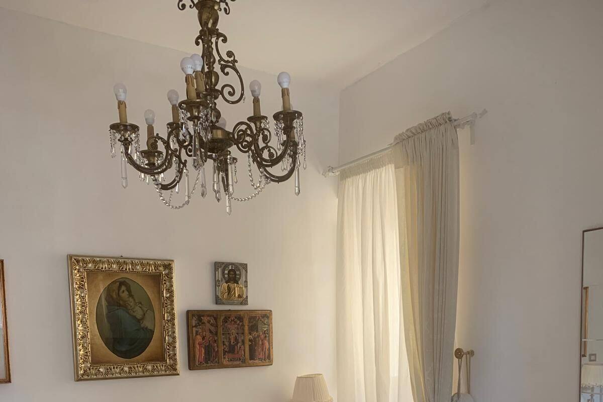 A bedroom with a large bed, a chandelier, a bedside table with a lamp, and a mirror on the wall.