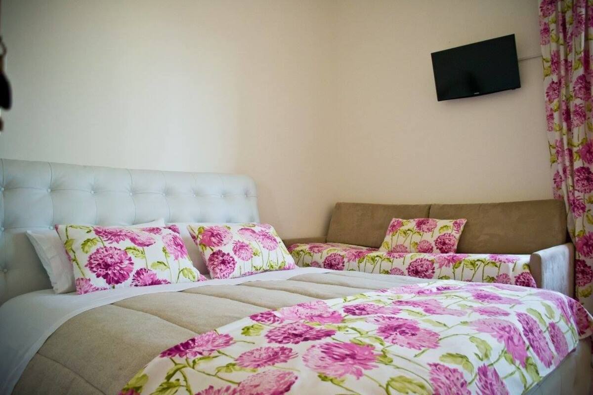 A bedroom with a tufted headboard, floral bedding, a flat-screen TV mounted on the wall, and a curtain with a floral pattern.