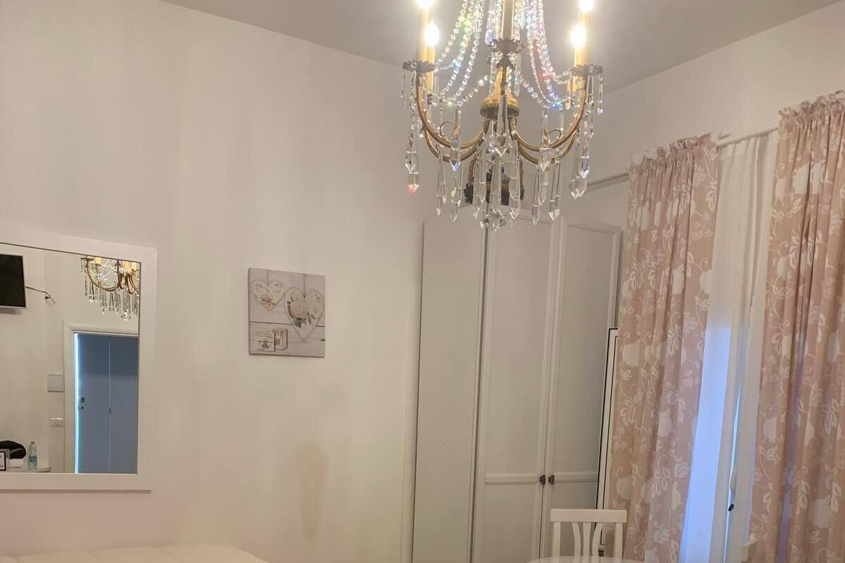 A bedroom with two beds, a chandelier, a mirror, a wardrobe, and a small table with chairs.