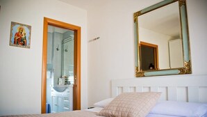 Quarto com uma cama, um espelho grande, uma porta para um banheiro e um ícone religioso na parede.