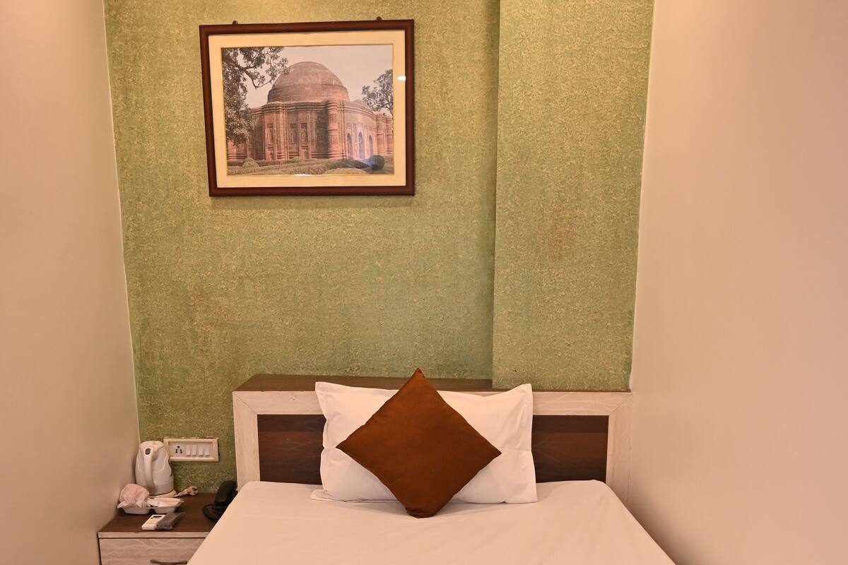 Una habitación de hotel con una cama bien hecha, un cuadro en la pared y una mesita de noche con un teléfono y una lámpara.
