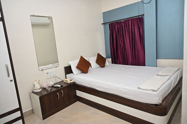 A bedroom with a bed, a nightstand, a mirror, a window with curtains, and a wall-mounted air conditioner.
