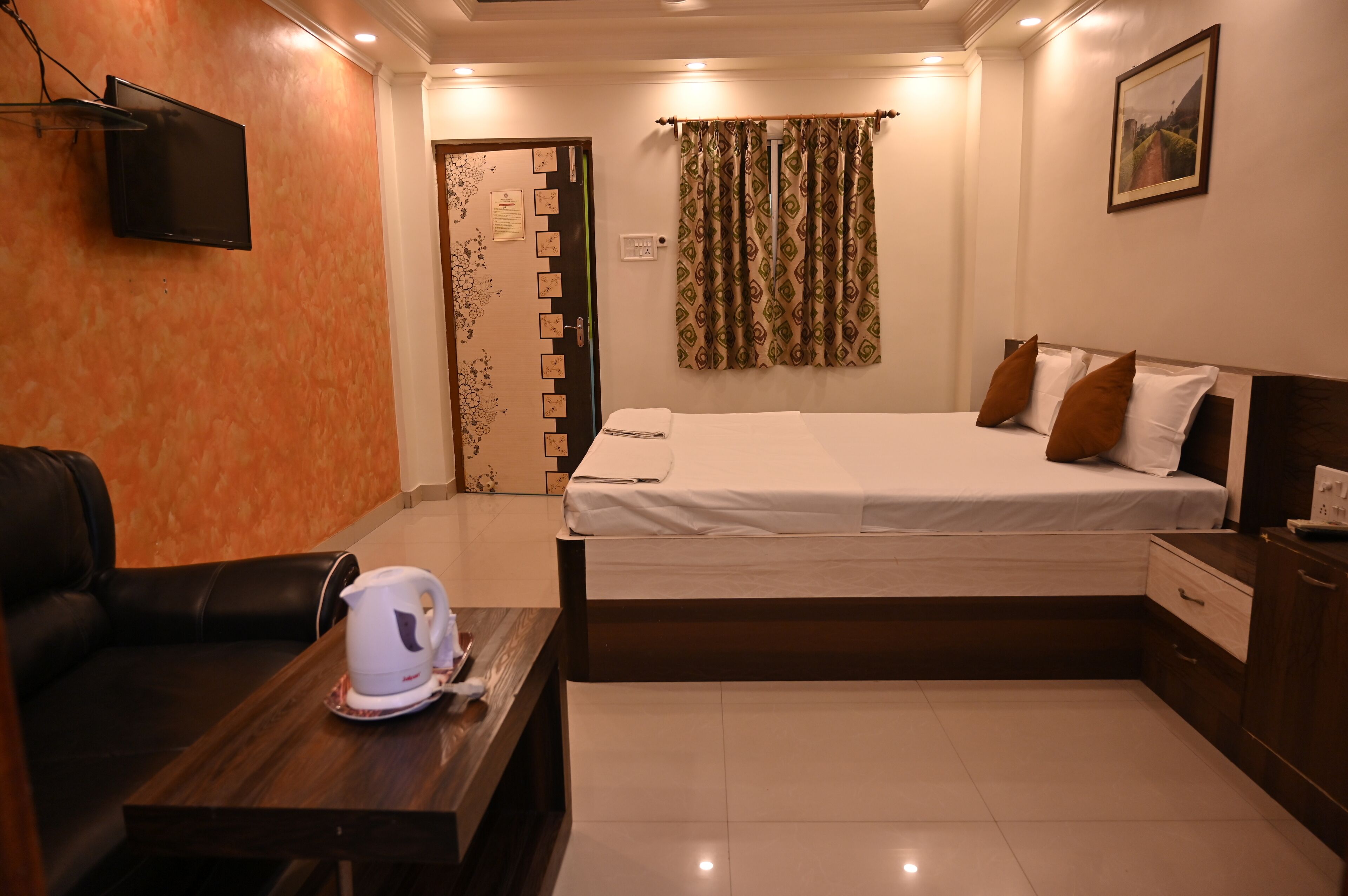 A hotel room with a bed, a desk with a kettle, a TV, and a door with a lock.