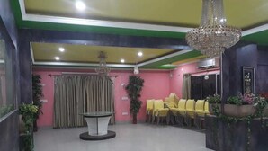 Un hall d’hôtel avec un comptoir d’accueil, des chaises jaunes, un lustre et une plante en pot.
