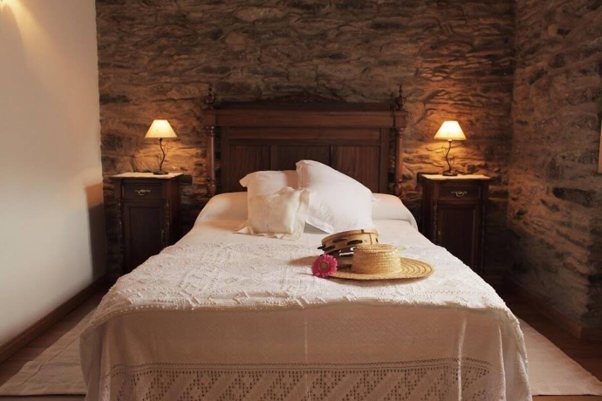 A bed with white linens, two bedside lamps, and a straw hat on the bed.