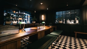 A bar area with a checkered floor, wooden bar counter, and seating.