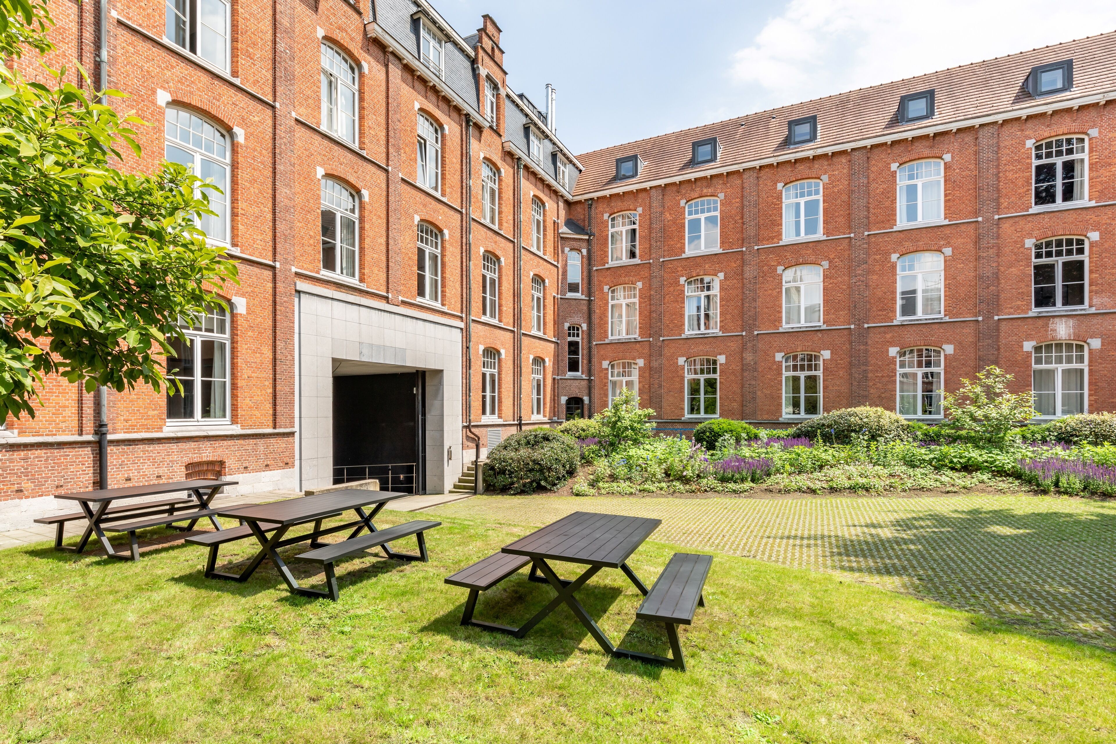 A courtyard with picnic tables and a brick building with multiple windows and a door.