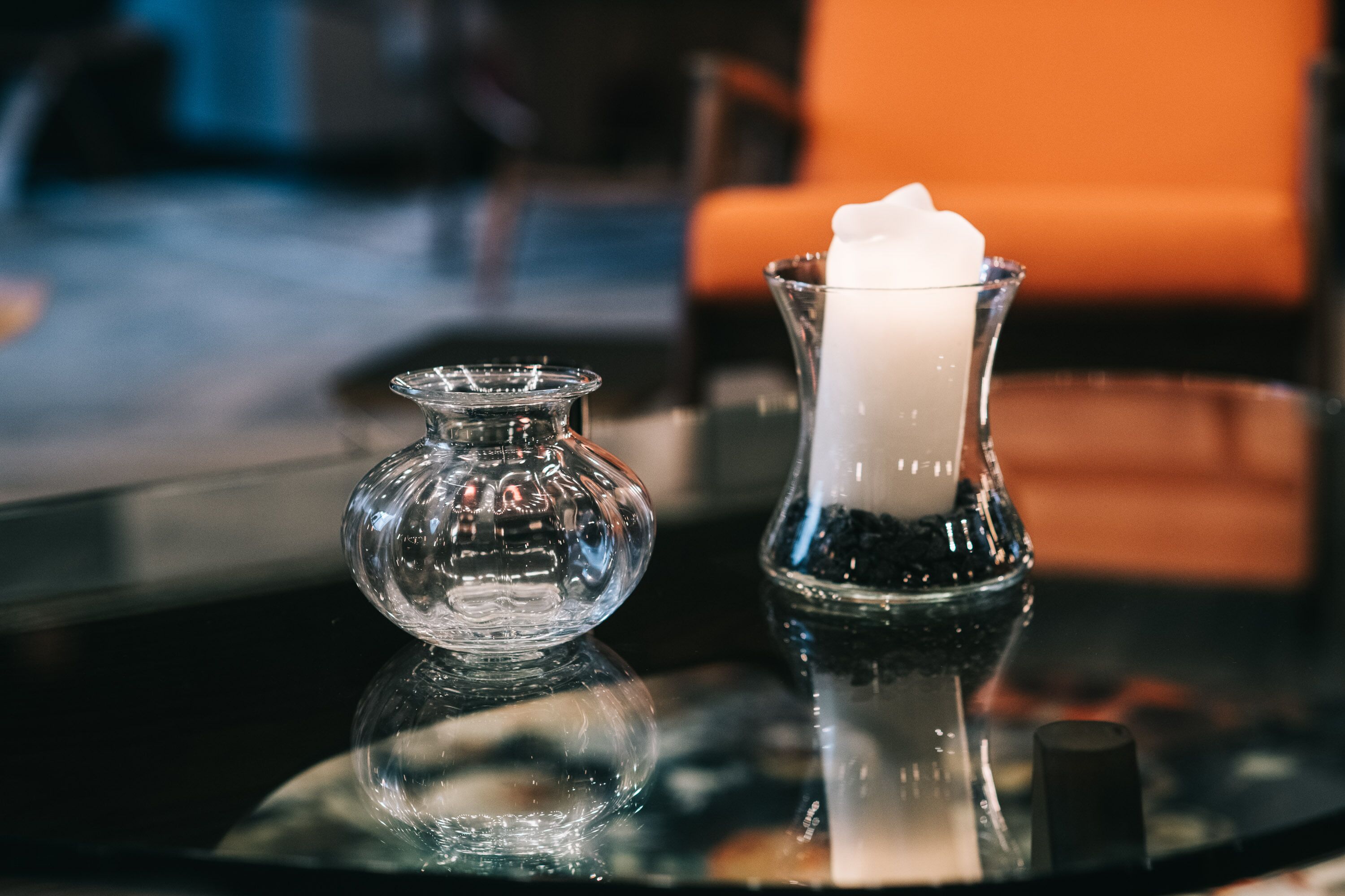 A glass candle holder with a white candle on a reflective surface.