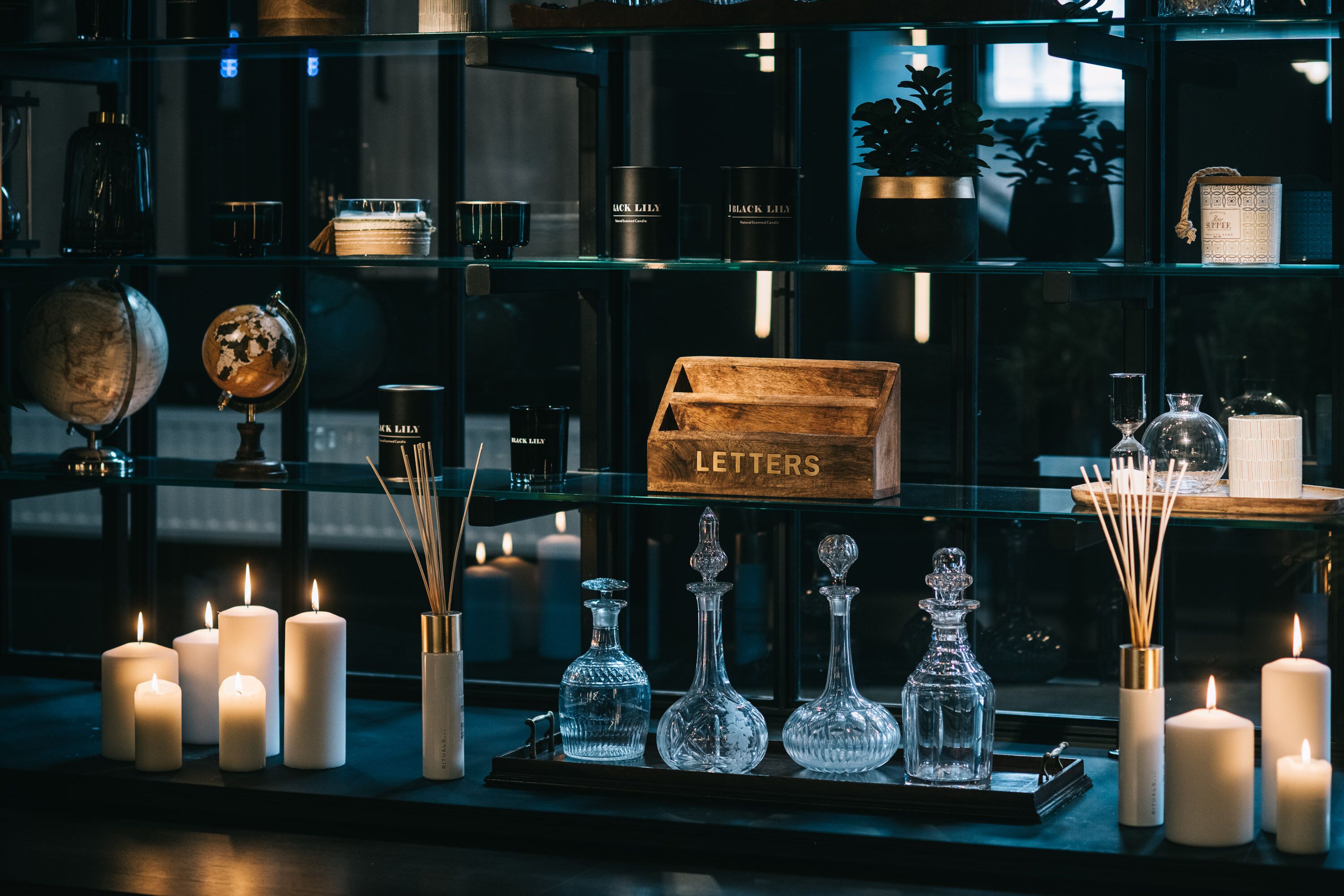 A display of candles, glassware, and a wooden box labeled "LETTERS" in a dimly lit room.