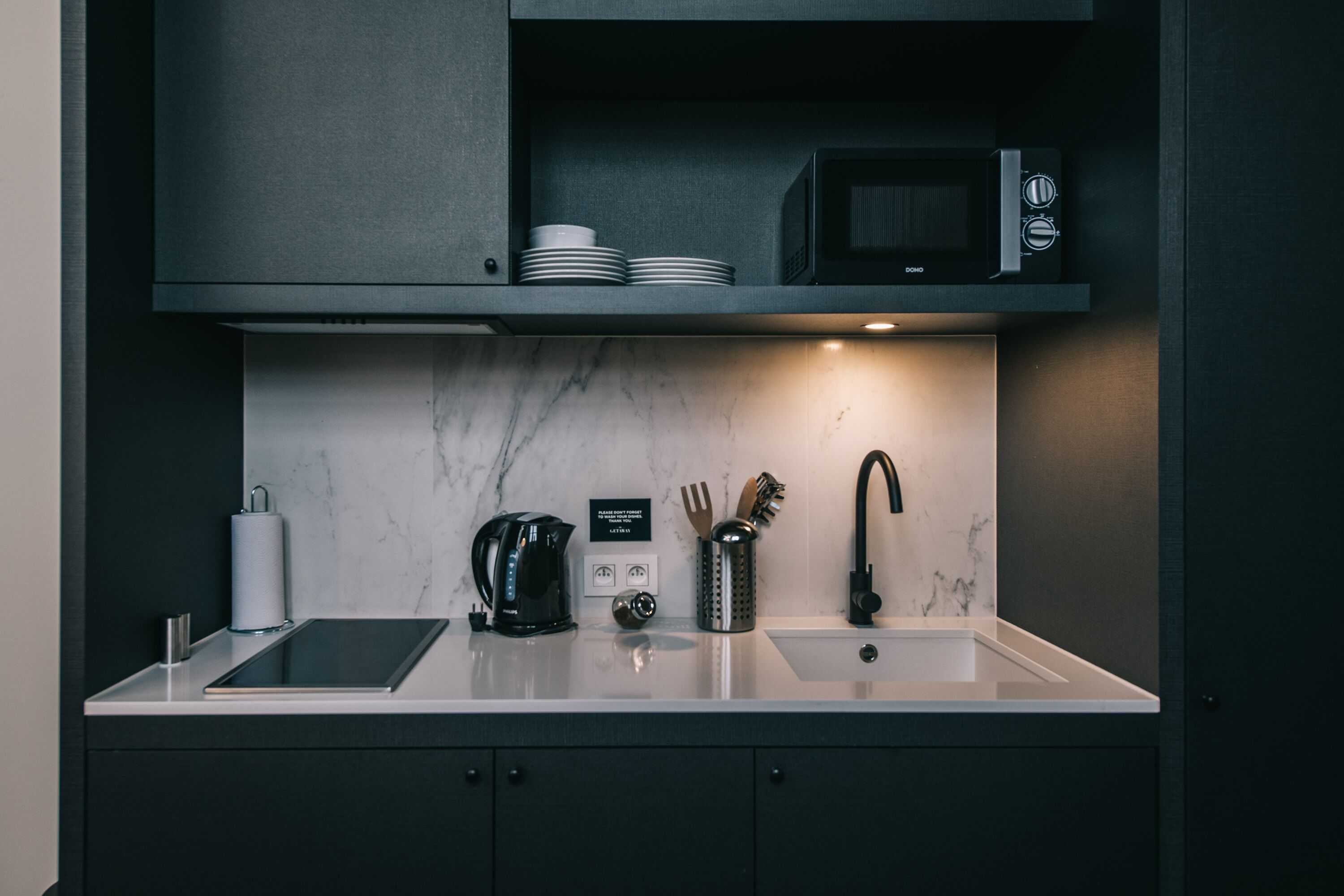 A modern kitchen with a marble countertop, a black coffee maker, a microwave, and a sink.