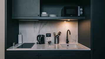 A modern kitchen with a marble countertop, a black coffee maker, a microwave, and a sink.
