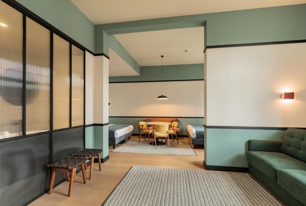 A modern interior with a sofa, a small table, and a bench. There is a window with blinds and a hanging light fixture.