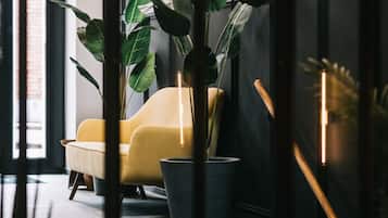 A modern interior with a yellow armchair, a large potted plant, and a staircase leading to an upper level.
