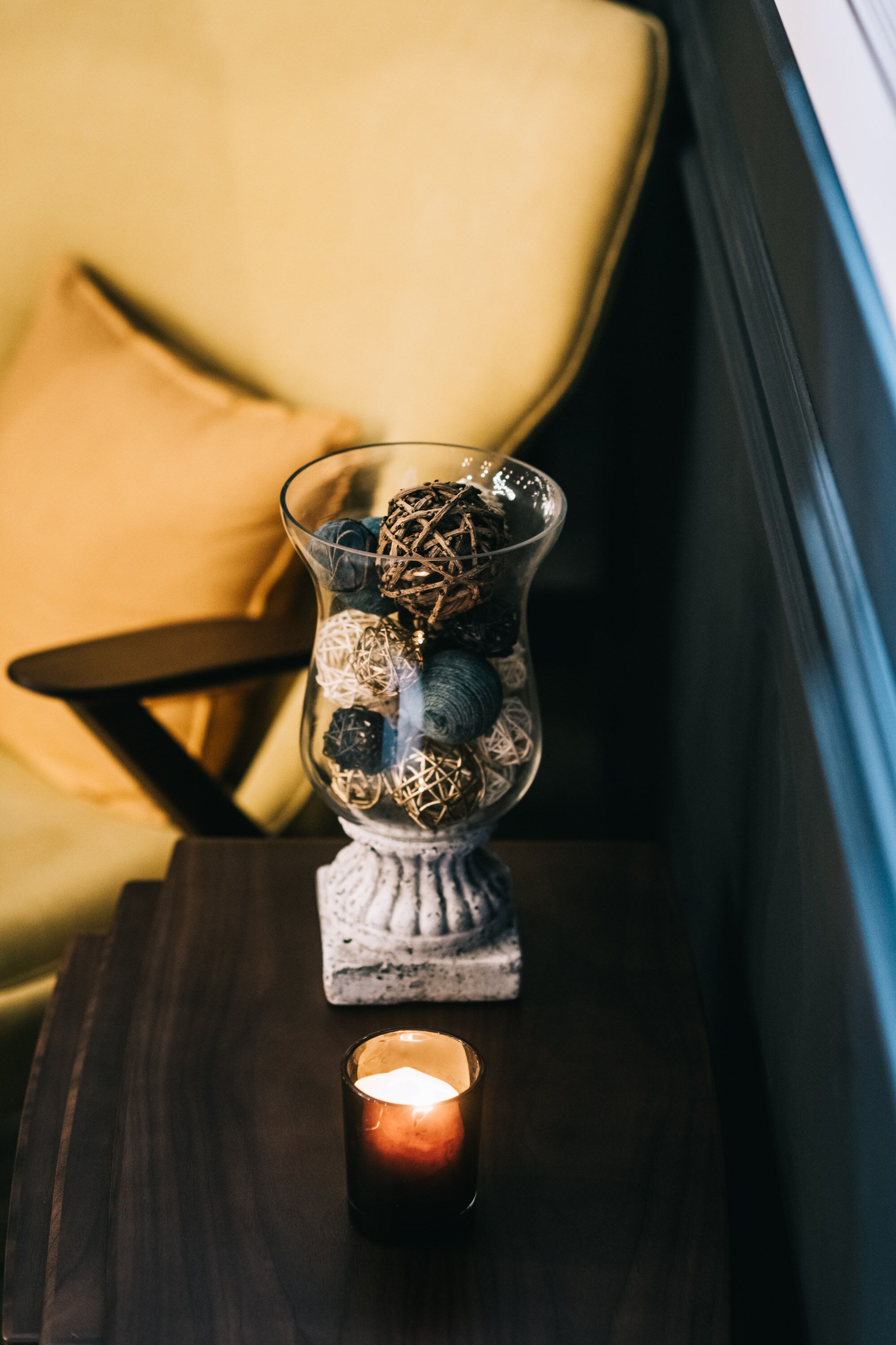 Un florero de vidrio con adornos sobre una mesa de madera junto a una silla con cojín.