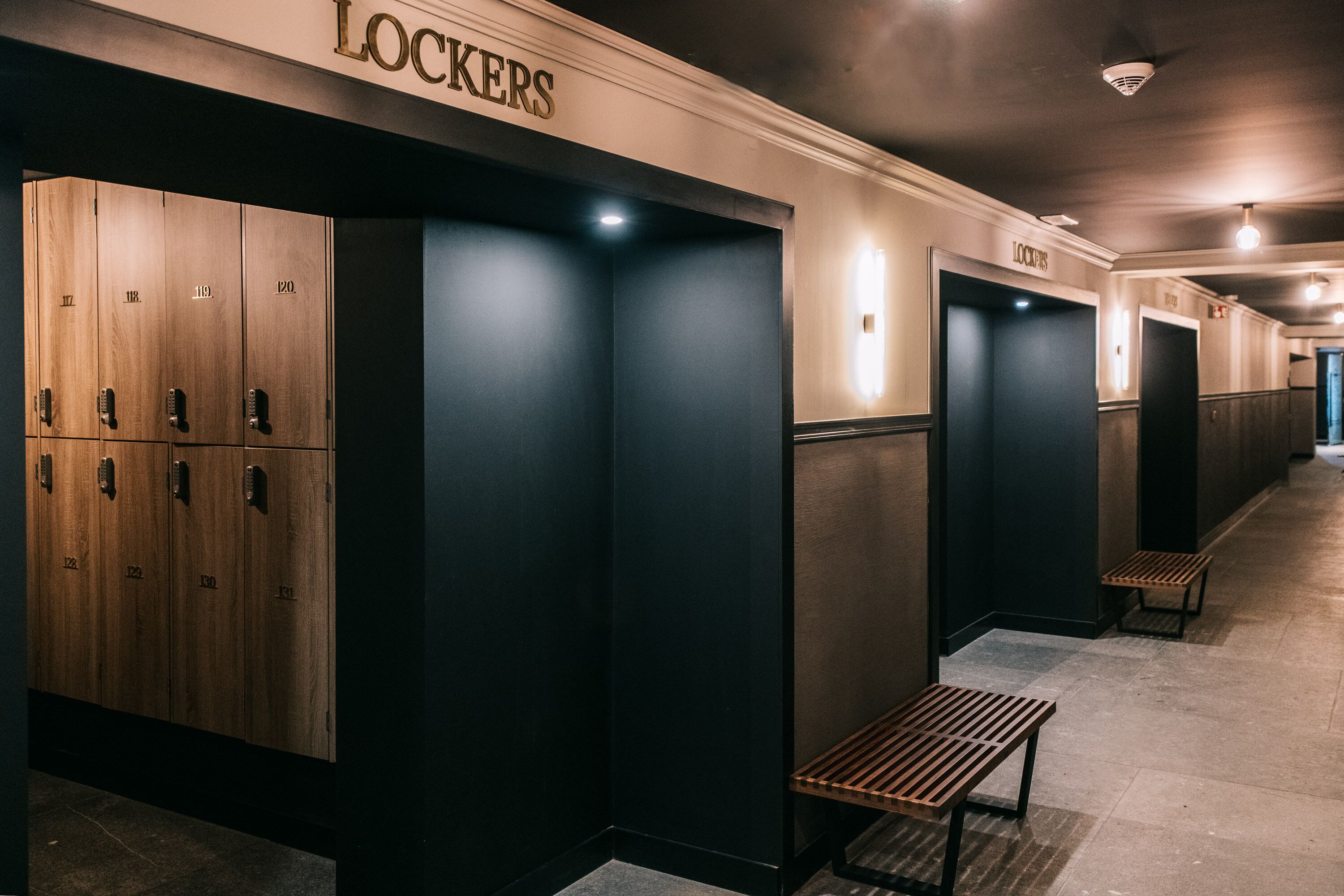 Un couloir d’hôtel avec des casiers, des bancs et un panneau indiquant « LOCALISATEURS ».