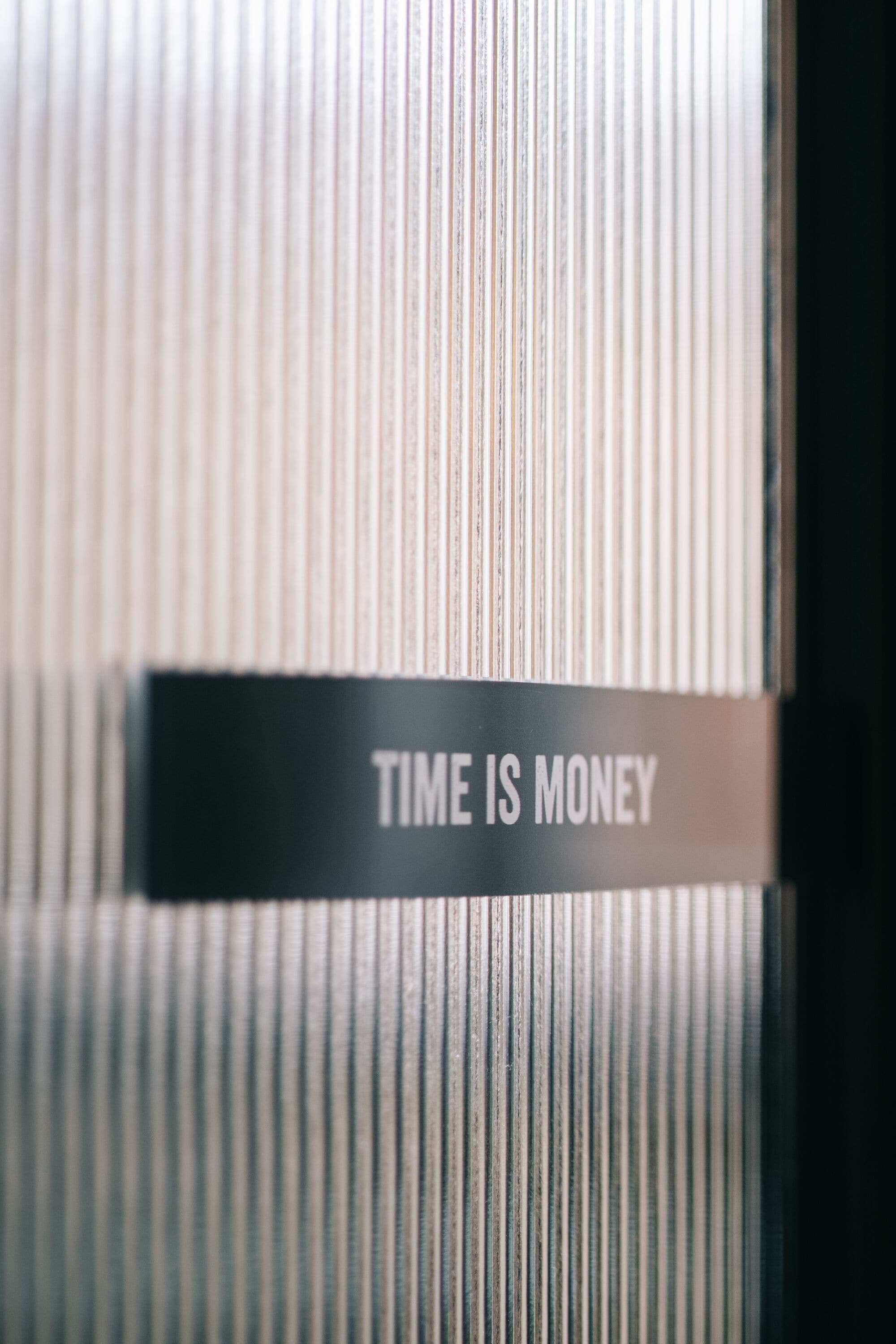 A close-up of a metallic sign with the text "TIME IS MONEY" against a background of vertical lines, likely part of a larger structure or wall.