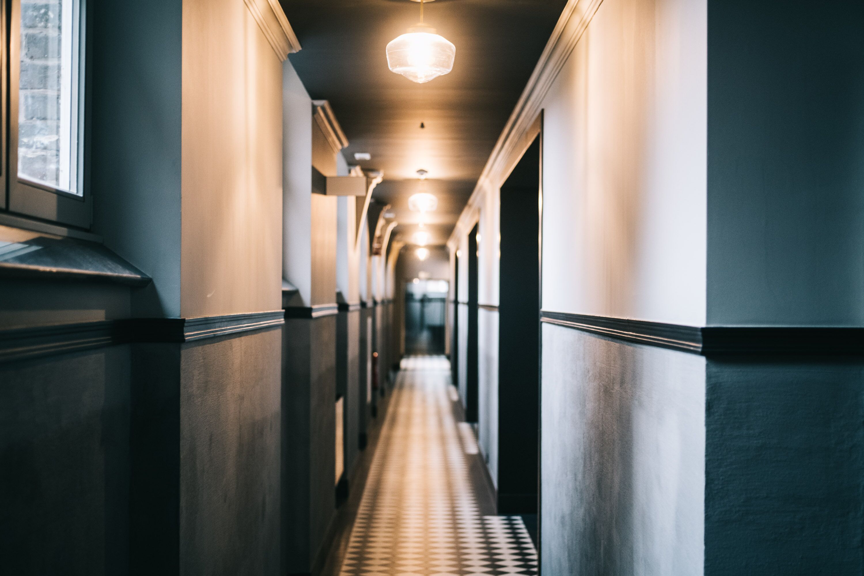 A long, narrow hallway with a patterned floor, flanked by walls with a dark finish and a light-colored trim.