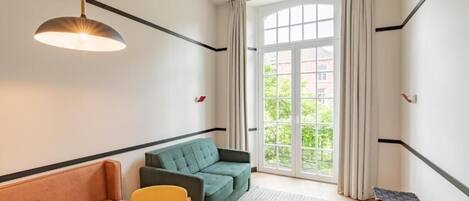 A modern living room with a sofa, a chair, a small table, and a large window with curtains.