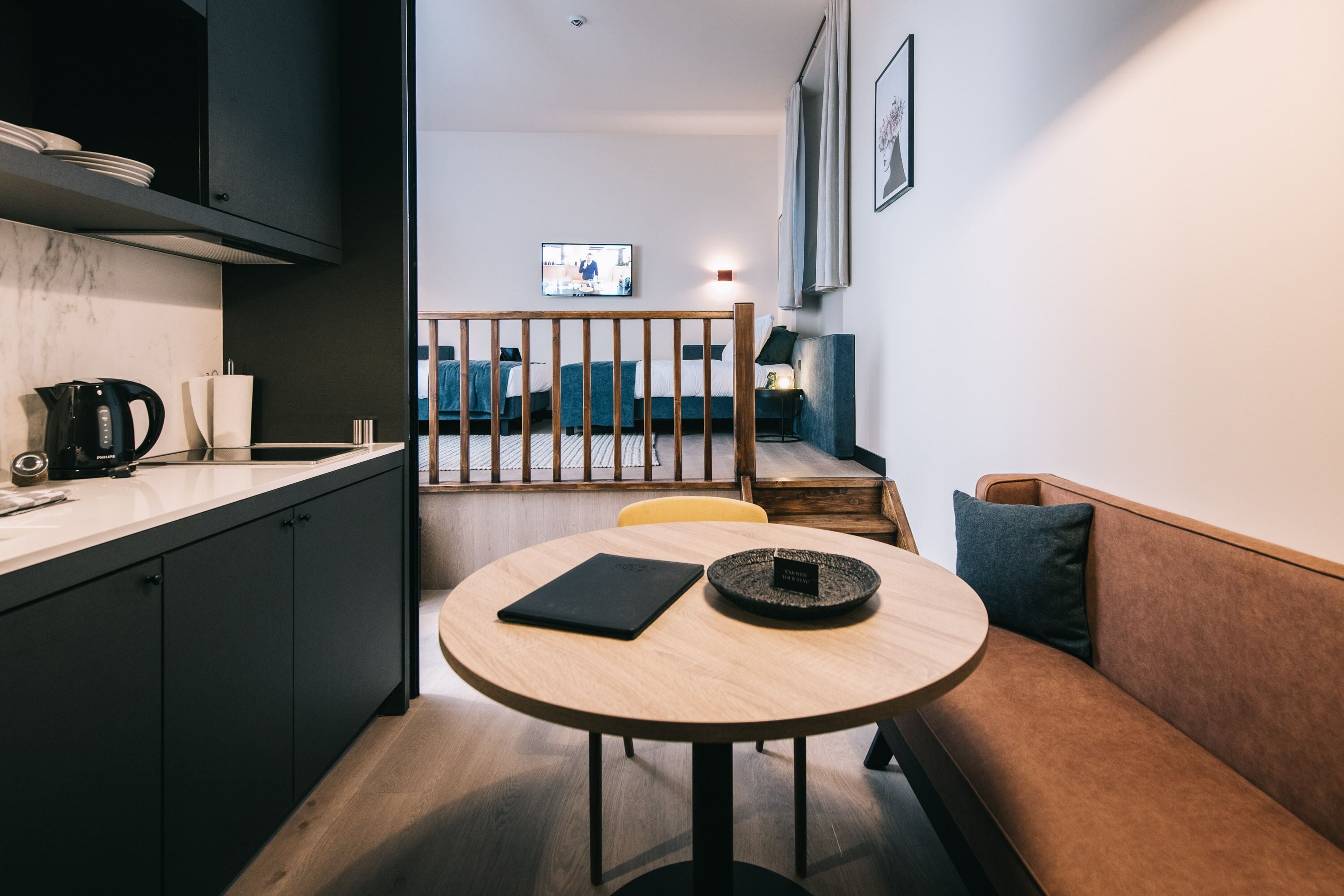 A modern kitchen with dark cabinetry, a round wooden table, and a sofa with cushions.