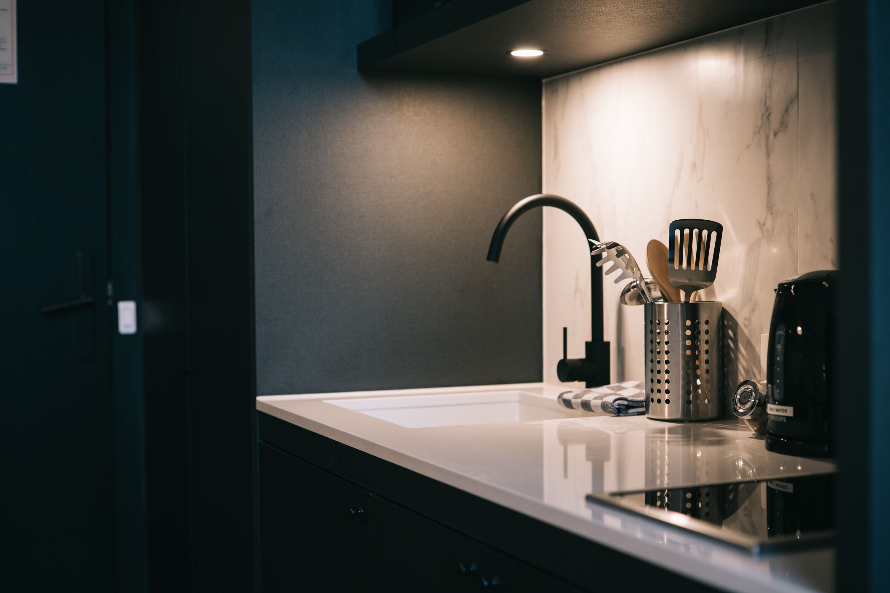 Una cucina moderna con un piano di lavoro bianco, un rubinetto nero, una macchina da caffè e un portauovili.