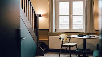 Une pièce avec un escalier en bois, une table ronde entourée de chaises, un radiateur et une fenêtre avec des rideaux.