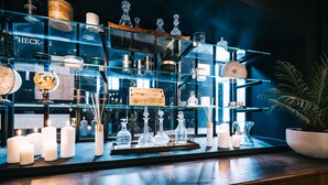 Zona de bar con estanterías que exhiben varias botellas y vasos, una planta en maceta y velas.