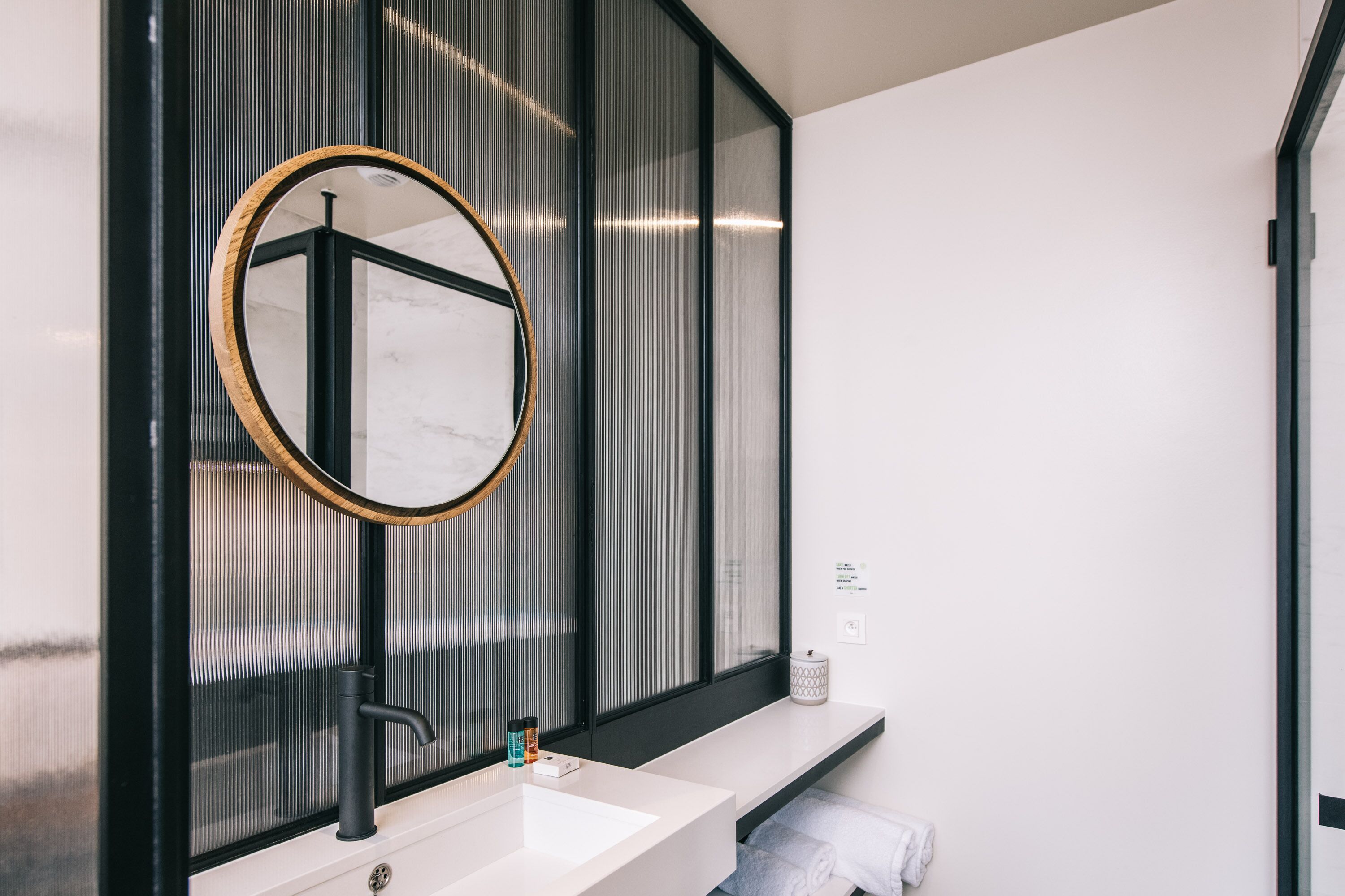 Une salle de bain moderne avec un grand miroir, un lavabo blanc et un porte-serviettes.