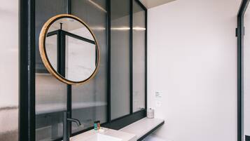 Une salle de bain moderne avec un grand miroir, un lavabo blanc et un porte-serviettes.