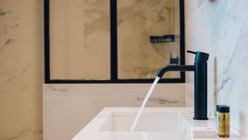 A modern bathroom with a white sink, a black faucet, and a marble wall.