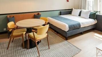 Une chambre d’hôtel moderne comprenant un lit, un canapé, une table à manger avec des chaises et un luminaire suspendu.