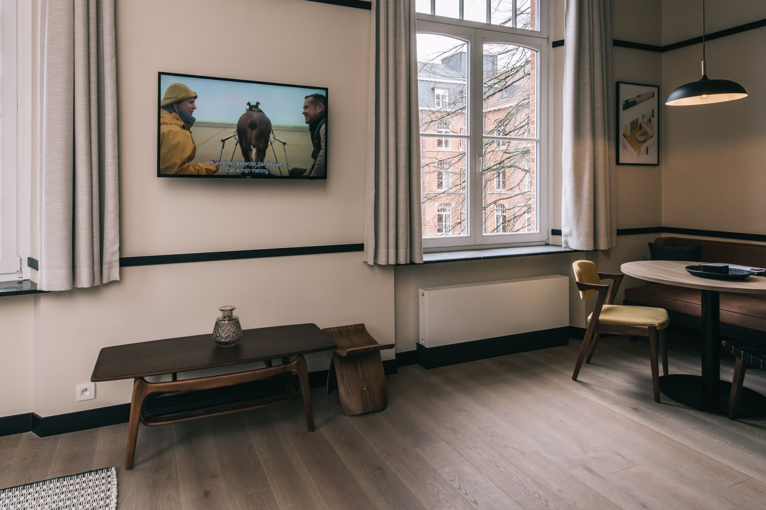 Una cocina moderna con un gran ventanal, piso de madera, una mesa de comedor con sillas y un televisor montado en la pared.