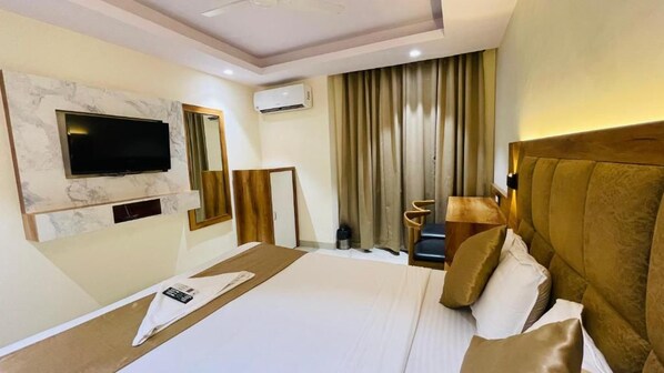 Habitación de hotel con cama, televisor montado en una pared de mármol, espejo, ventana con cortinas y cabecero.