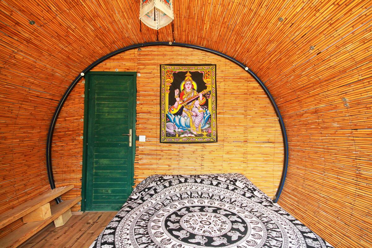 A room with a curved bamboo ceiling, a green door, and a tapestry with a circular pattern.