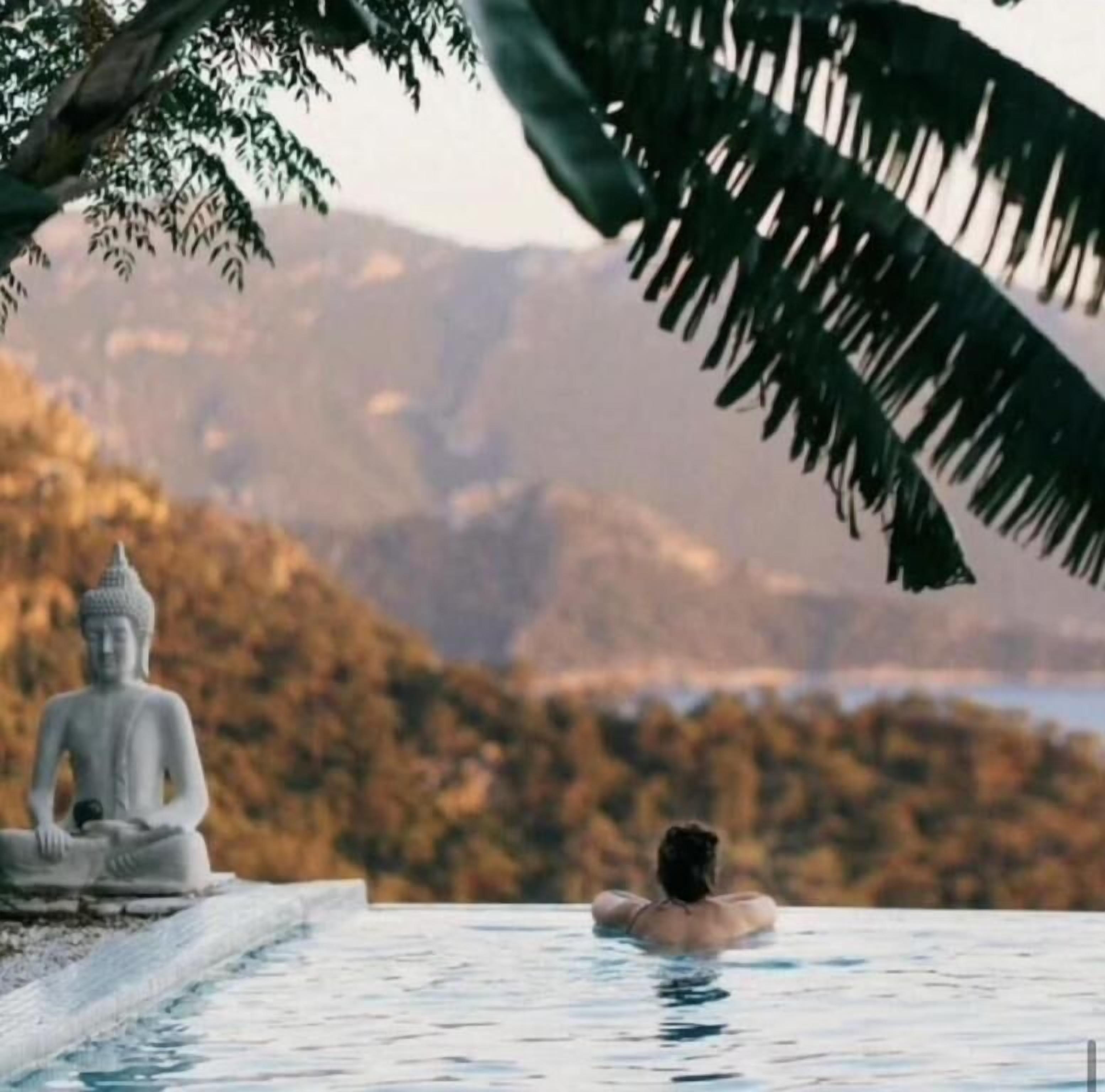 Una persona en una piscina con una estatua de Buda y montañas al fondo.