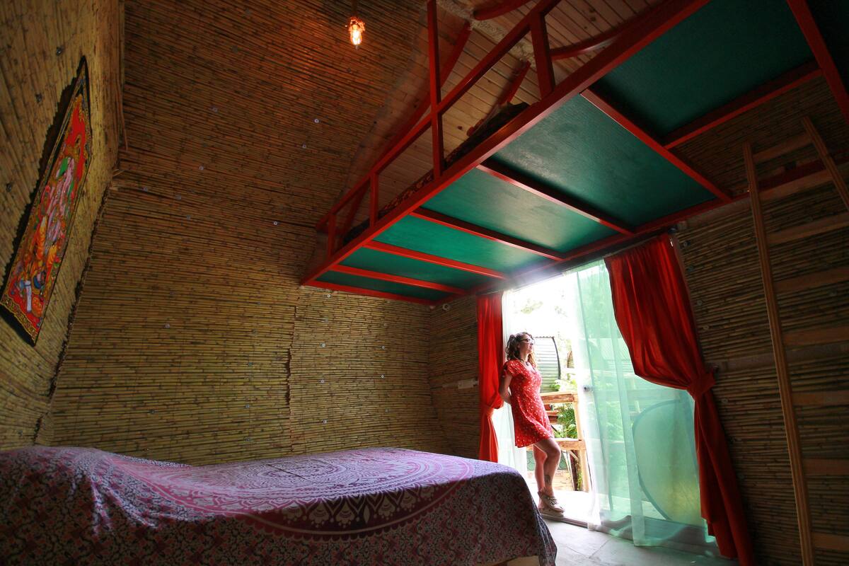 A room with a bed, a window with red curtains, and a wooden ceiling.
