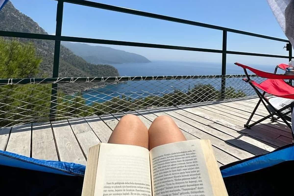 A person reclining in a hammock with a book, overlooking a scenic coastal view.