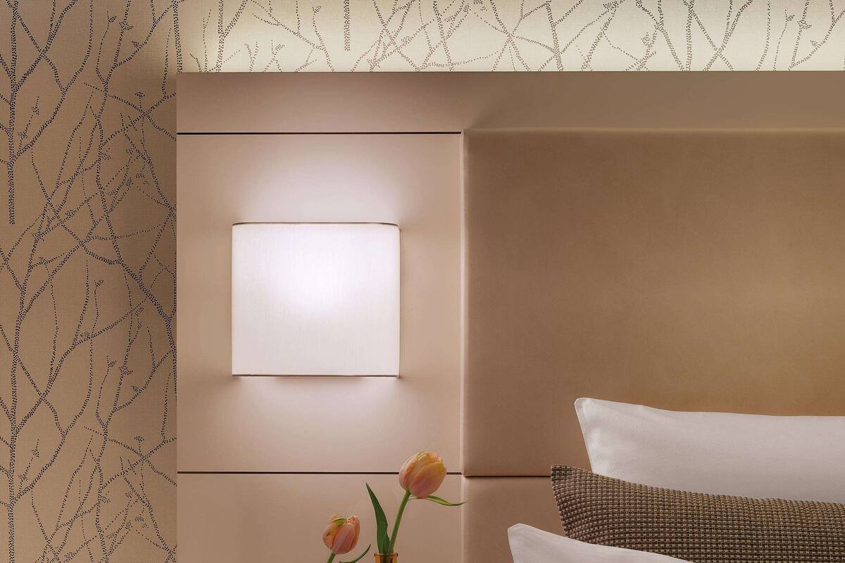 A neatly arranged hotel room with a bed, bedside table, and a wall-mounted light.