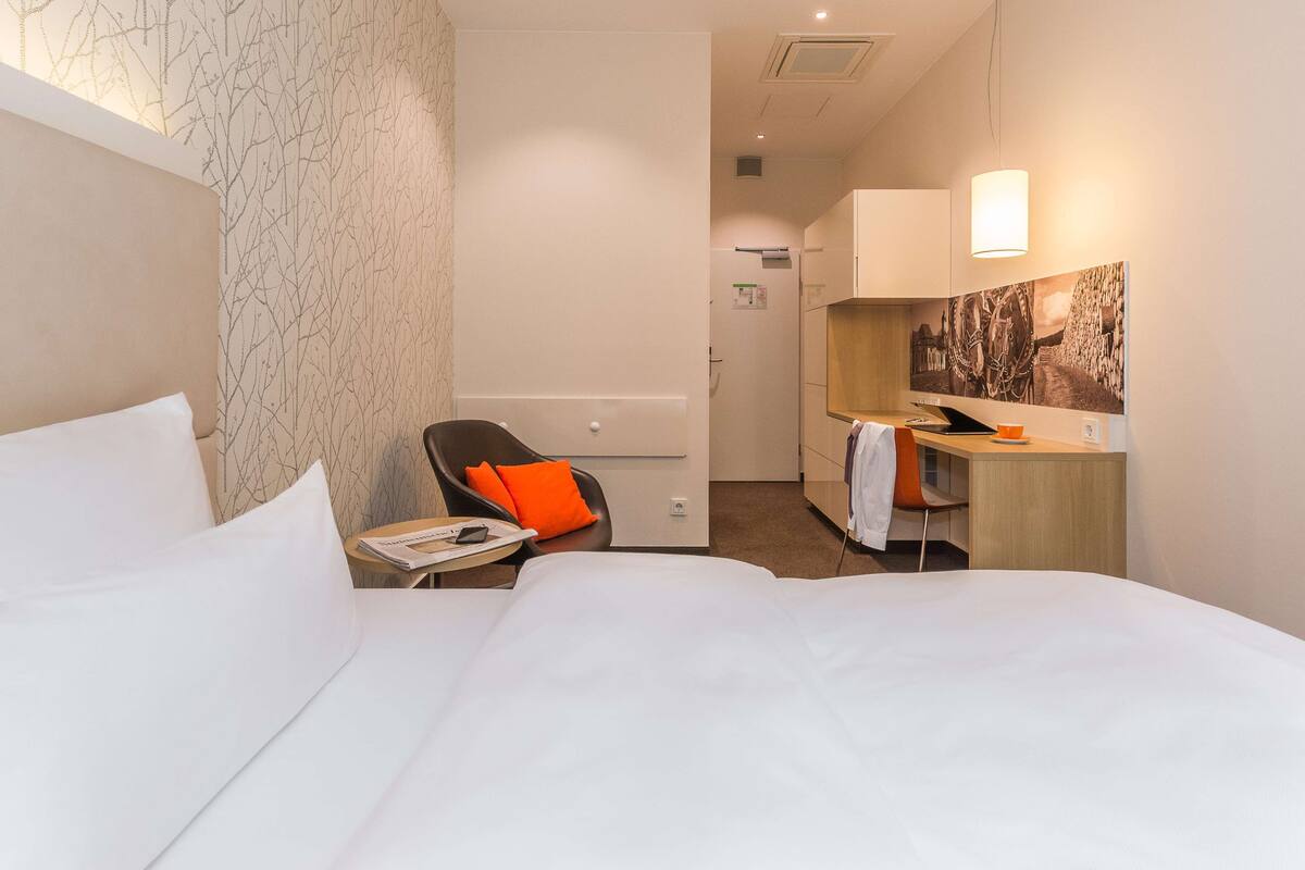 A hotel room with a bed, a desk, a chair, and a small table.