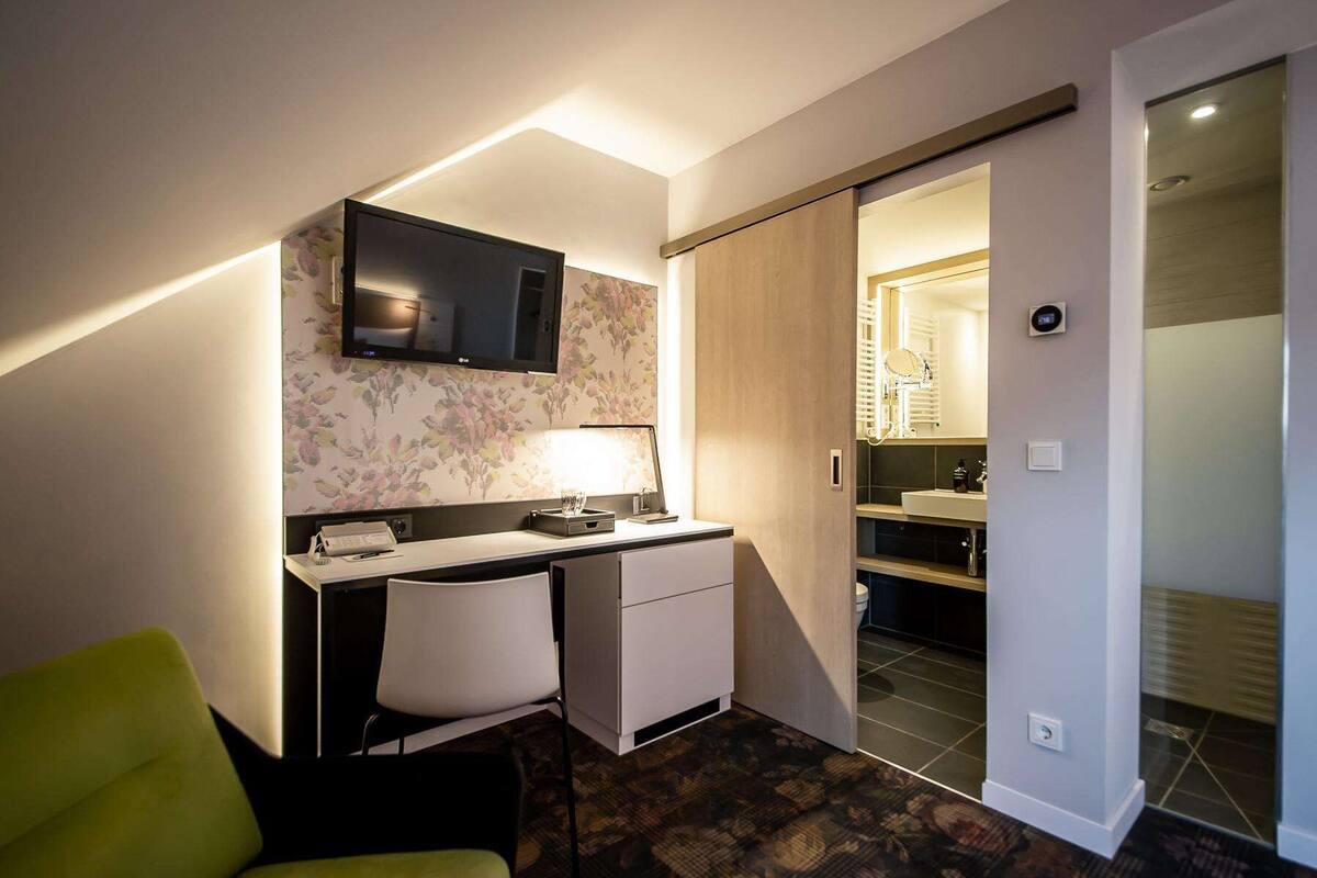 A compact hotel room with a desk, chair, and a television mounted on the wall.