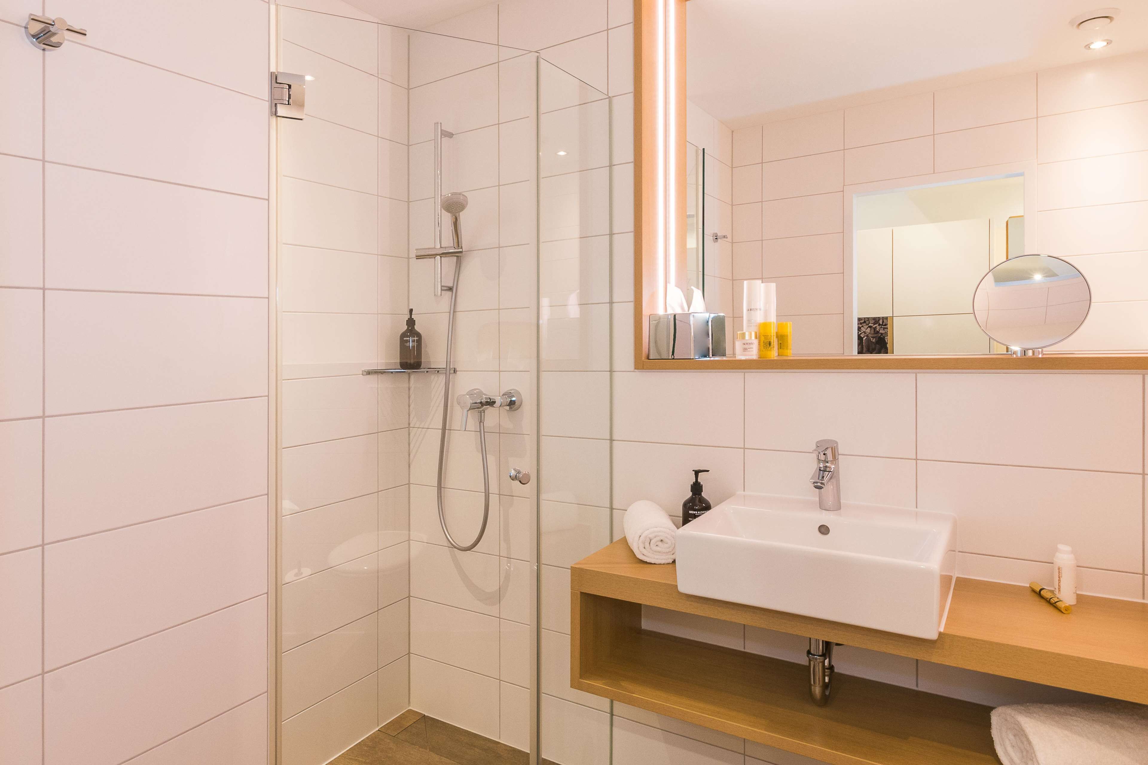 Un baño moderno con cabina de ducha de vidrio, lavabo blanco y tocador de madera, y un espejo sobre el lavabo.