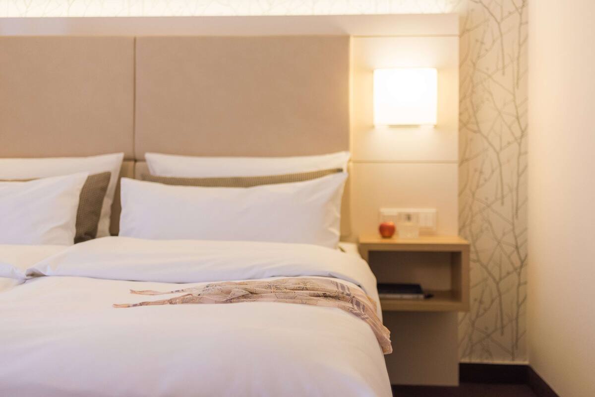 A hotel room with a bed, bedside tables, and a wall-mounted light.