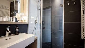 Et moderne badeværelse med en hvid vask, en glasbrusekabine og mørke flisevægge.
