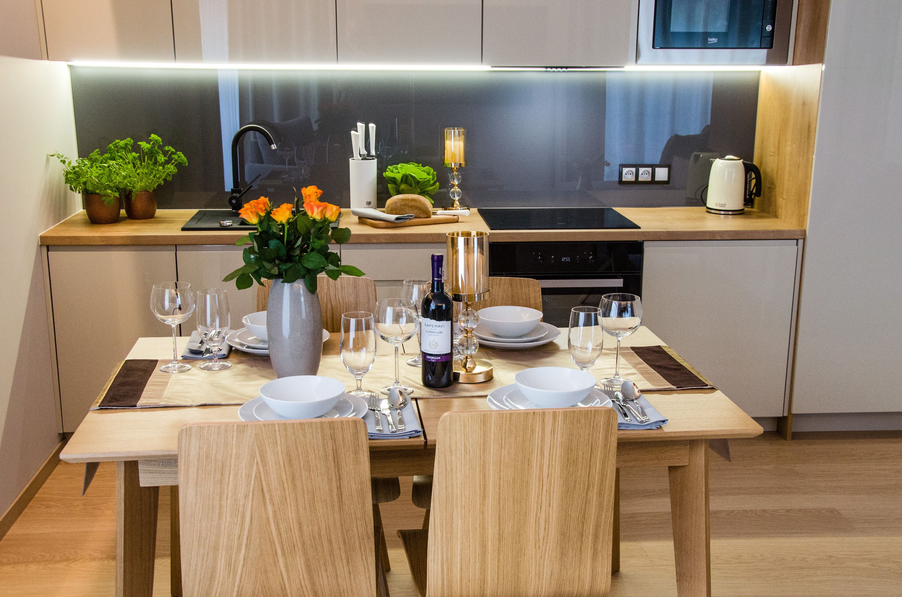 Et moderne køkken med et spisebord dækket til fire personer, komplet med vinglas, tallerkener og en vase med blomster.