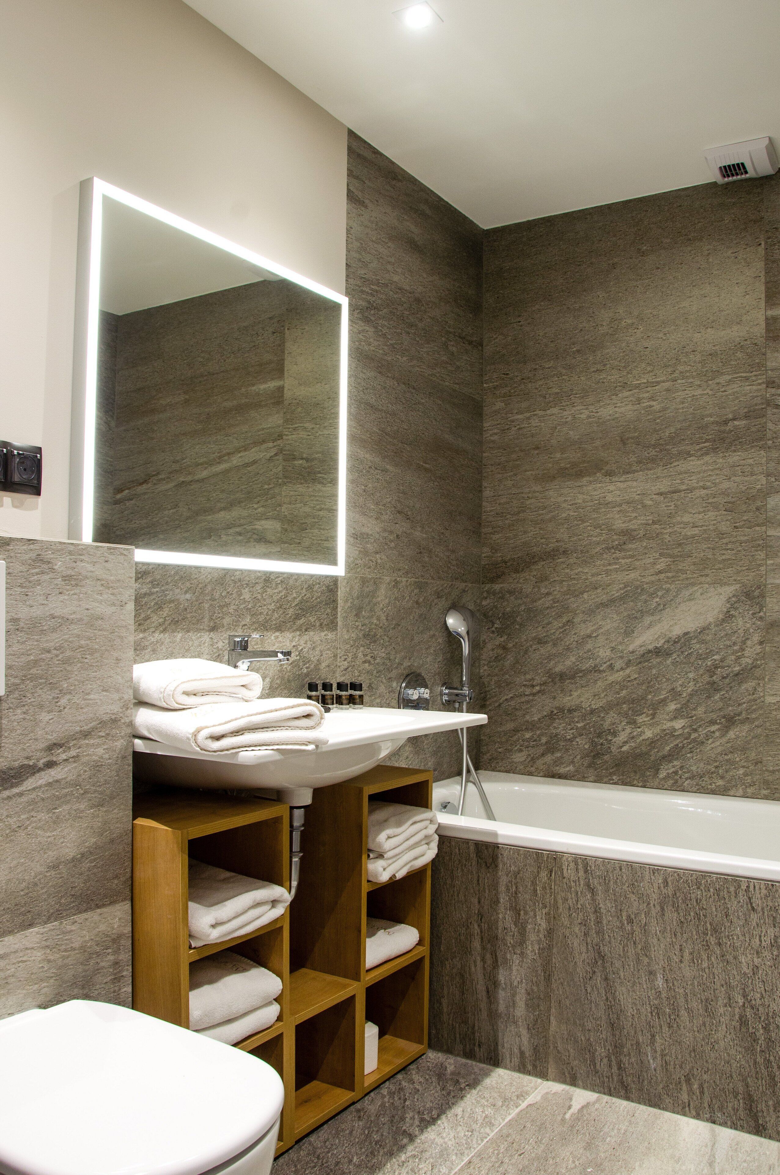 A modern bathroom with a marble wall, a large mirror, a sink, a toilet, and a bathtub.