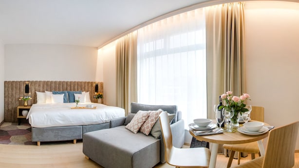 Une chambre d’hôtel moderne équipée d’un lit, d’un canapé, d’une table à manger avec des chaises et d’une grande fenêtre avec des rideaux.