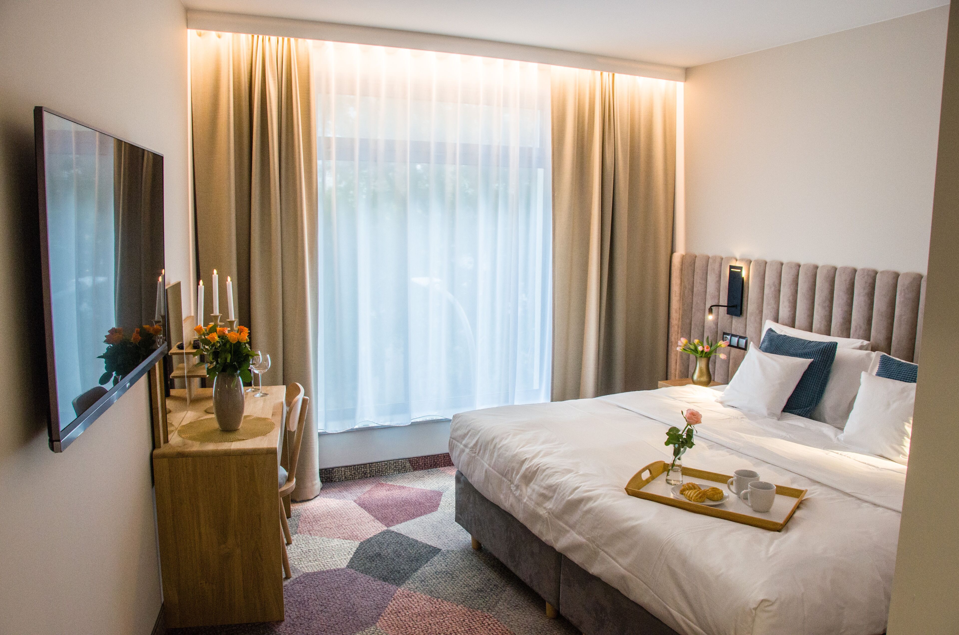 Una habitación de hotel con cama, mesita de noche y ventana con cortinas.