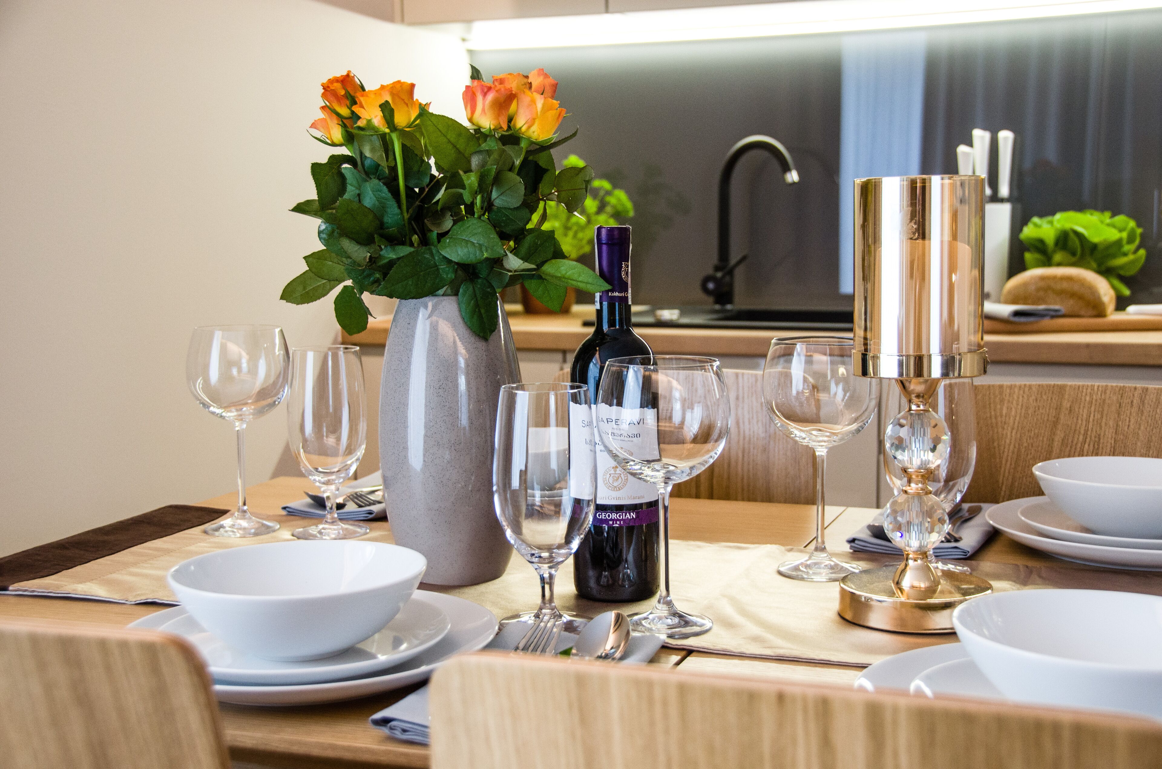 A dining table set with white bowls, wine glasses, and a bottle of wine.