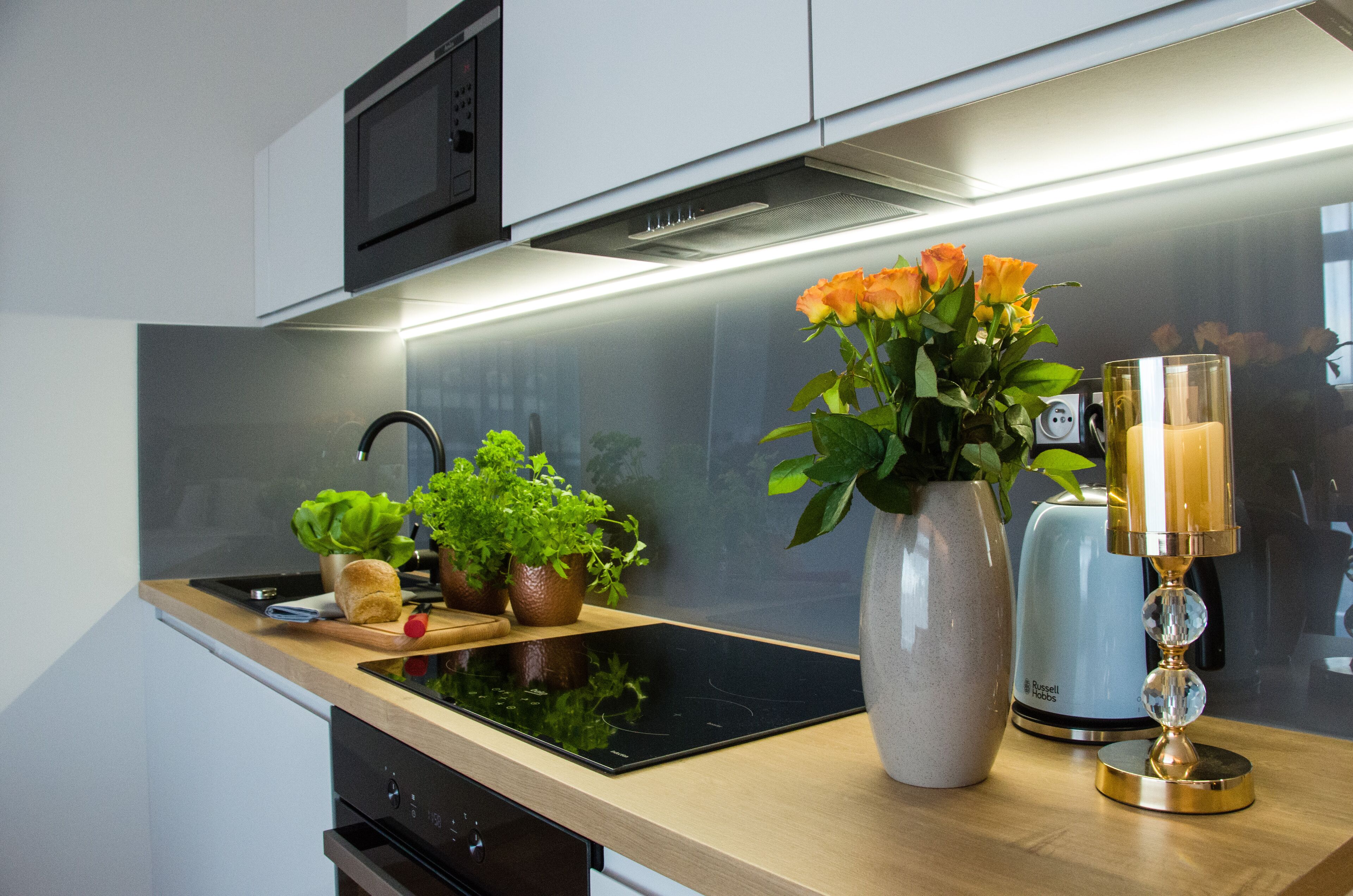 A modern kitchen with a built-in stove, a sink, and a countertop with potted plants and a vase of flowers.