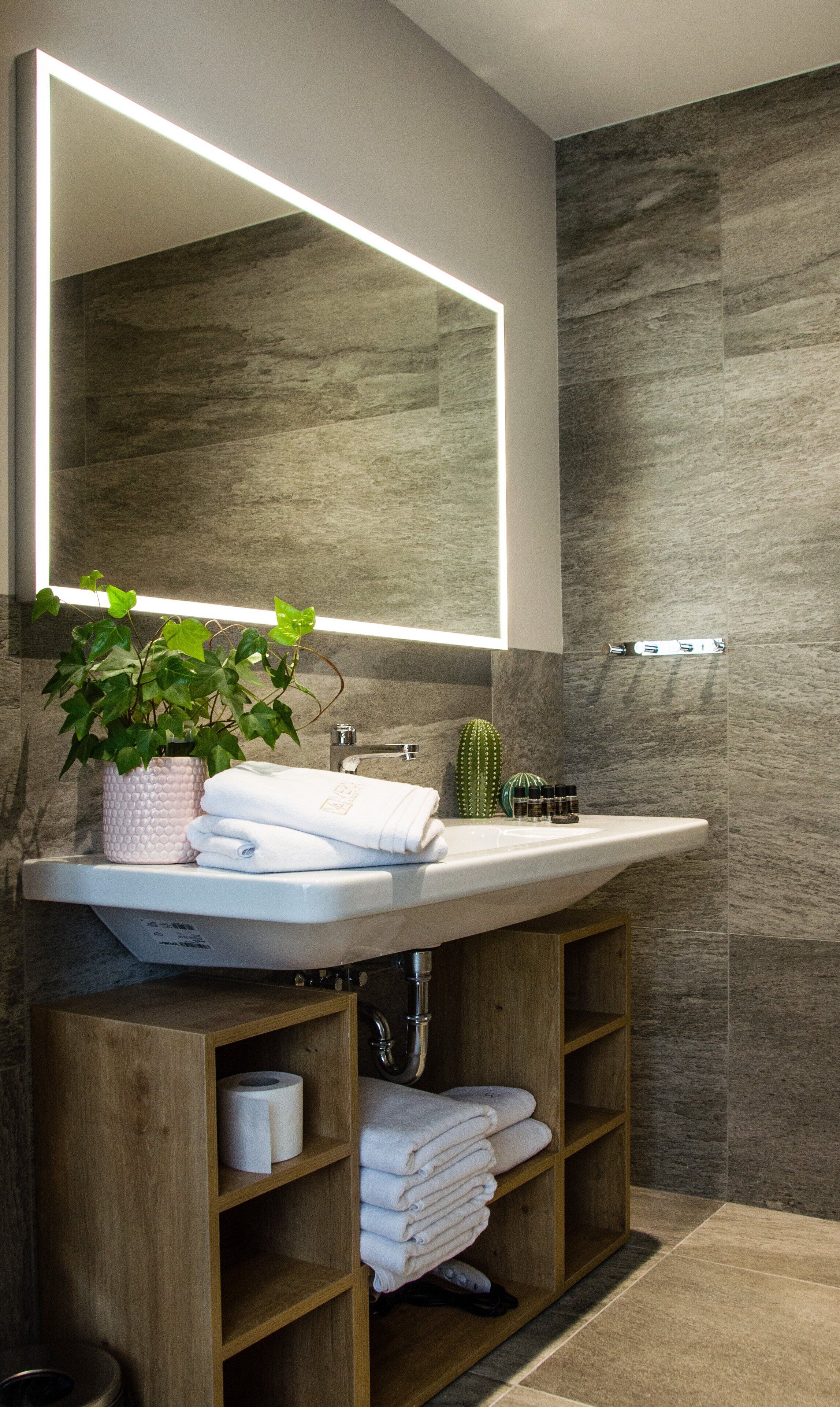 A modern bathroom with a large mirror, a sink, a potted plant, and neatly folded towels.